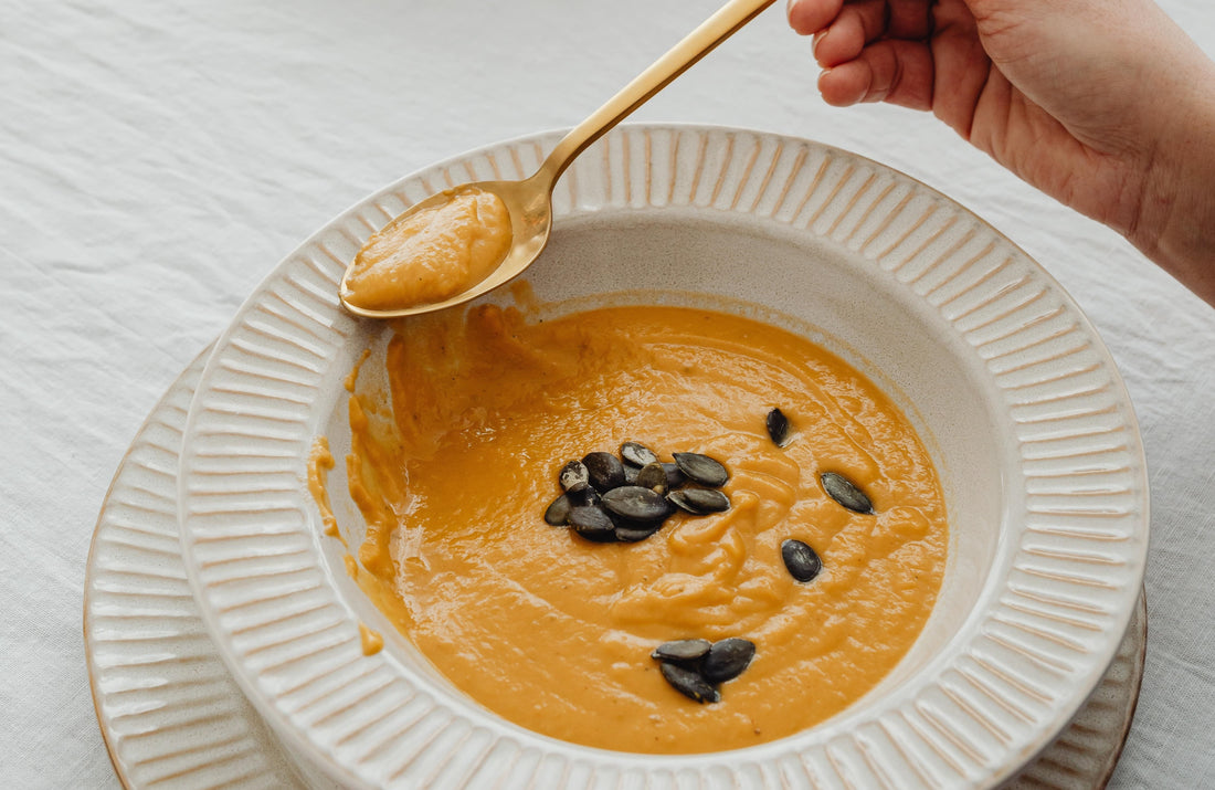 klassiek bord, soort Villeroy & Boch, met romige Pumpkin Spice Soep met geroosterde pompoenpitten, gouden lepel
